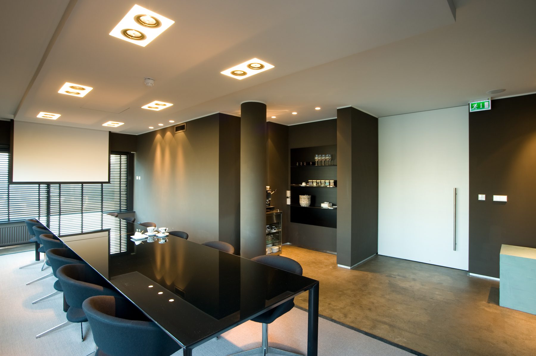 Vergaderzaal van hotel Elzenduin met lange tafel, ingebouwd projectiescherm en koffiehoek in de wand
