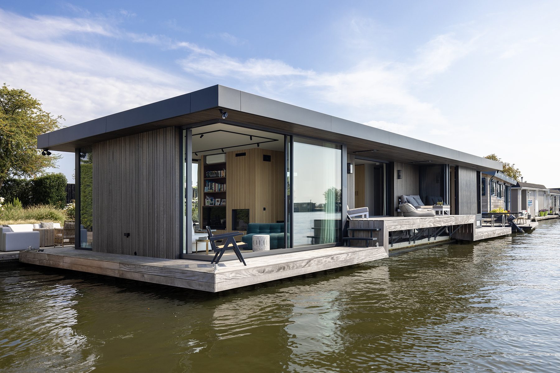 Moderne woonark aan de Vecht bij Weesp gezien vanaf het water, met donkere houten gevel, doorlopende glaspui en vlonderterras